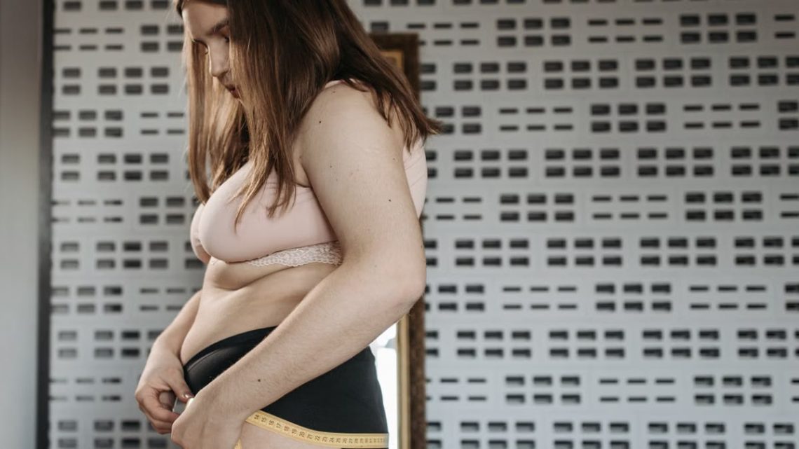 Confident young woman measures her hips in a stylish interior, embracing body positivity.