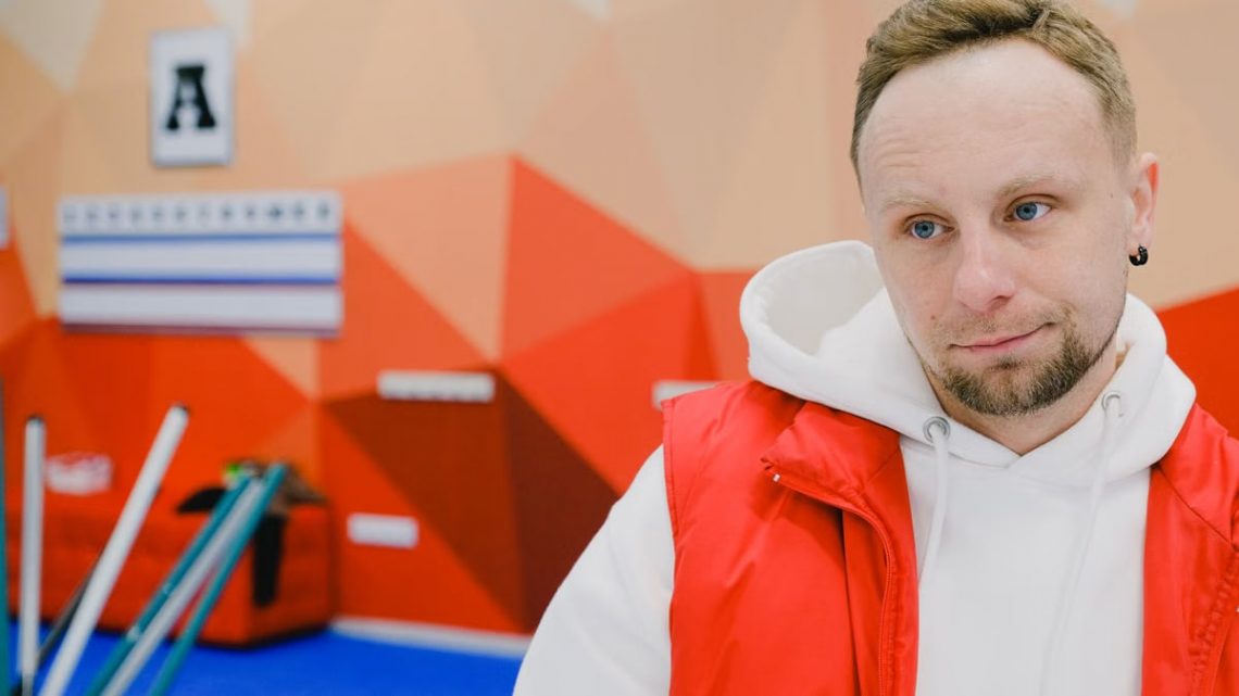 Serious male curling player in sportswear looking away with pensive face while standing near brooms and score board during game