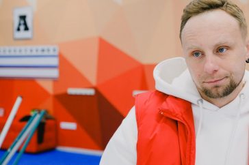 Serious male curling player in sportswear looking away with pensive face while standing near brooms and score board during game