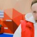 Serious male curling player in sportswear looking away with pensive face while standing near brooms and score board during game