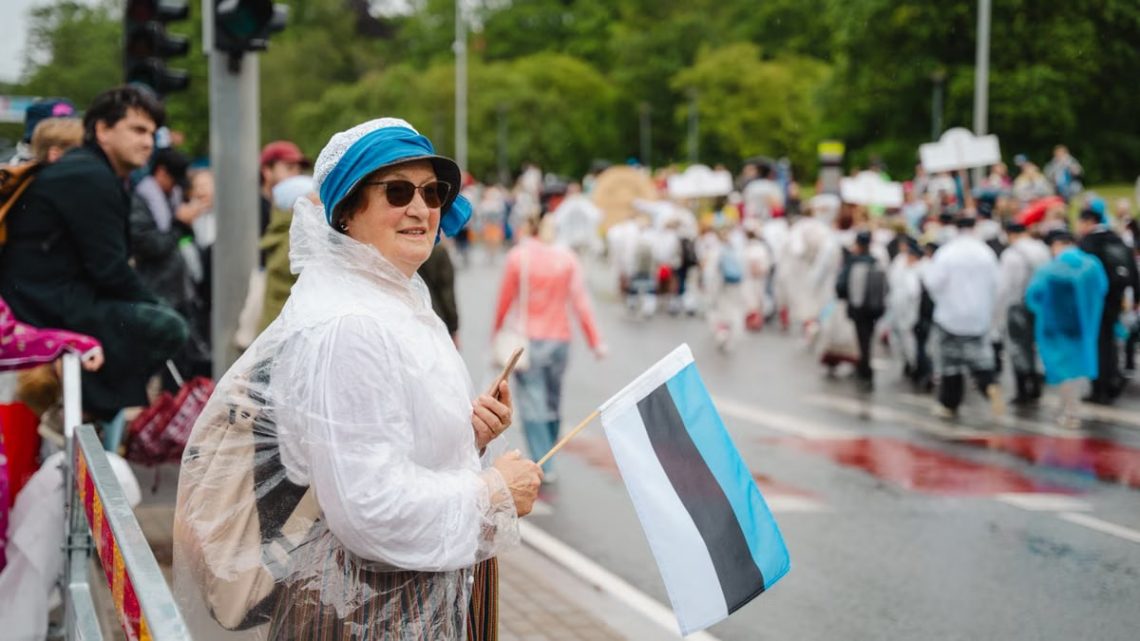 Woman enjoying a parade in Estonia, waving the Estonian flag amidst a lively crowd.