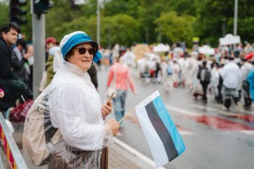 Woman enjoying a parade in Estonia, waving the Estonian flag amidst a lively crowd.