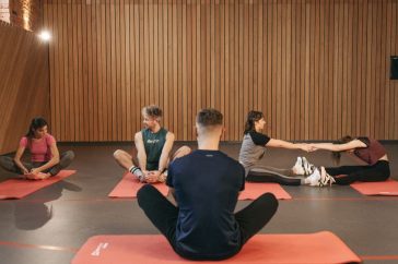 A group of adults practicing yoga and stretching on mats in a wooden panelled room.