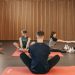 A group of adults practicing yoga and stretching on mats in a wooden panelled room.